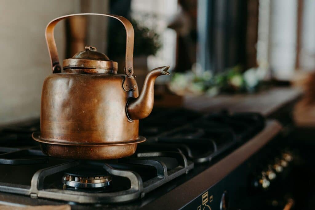 Bronze kettle in modern kitchen. Old vintage teapot on gas stove. Preparing tea